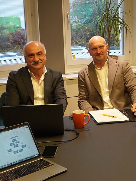 Två representanter diskuterar ISO-certifiering vid mötesbord med laptop