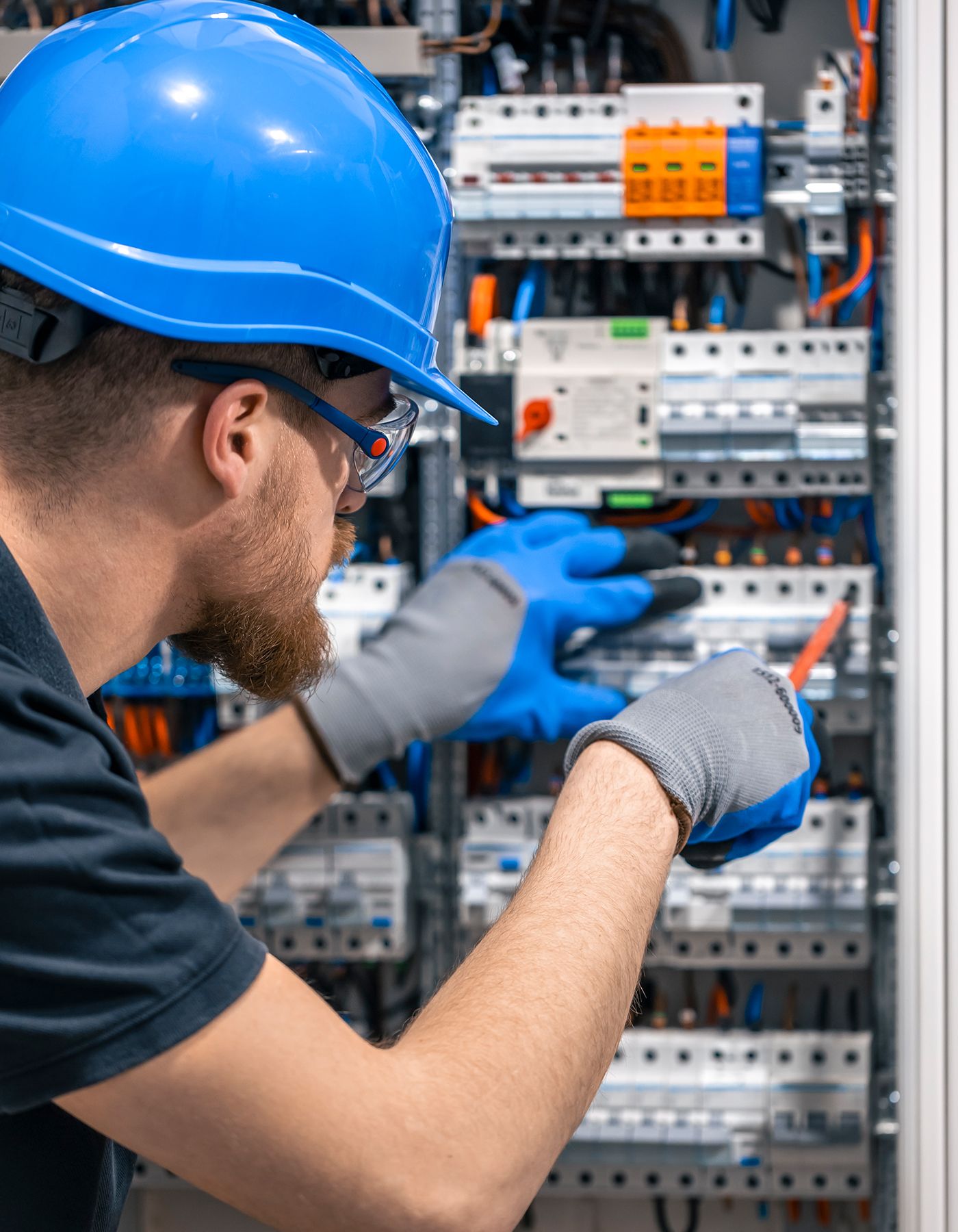 Elektriker i blå hjälm arbetar med säkringscentral