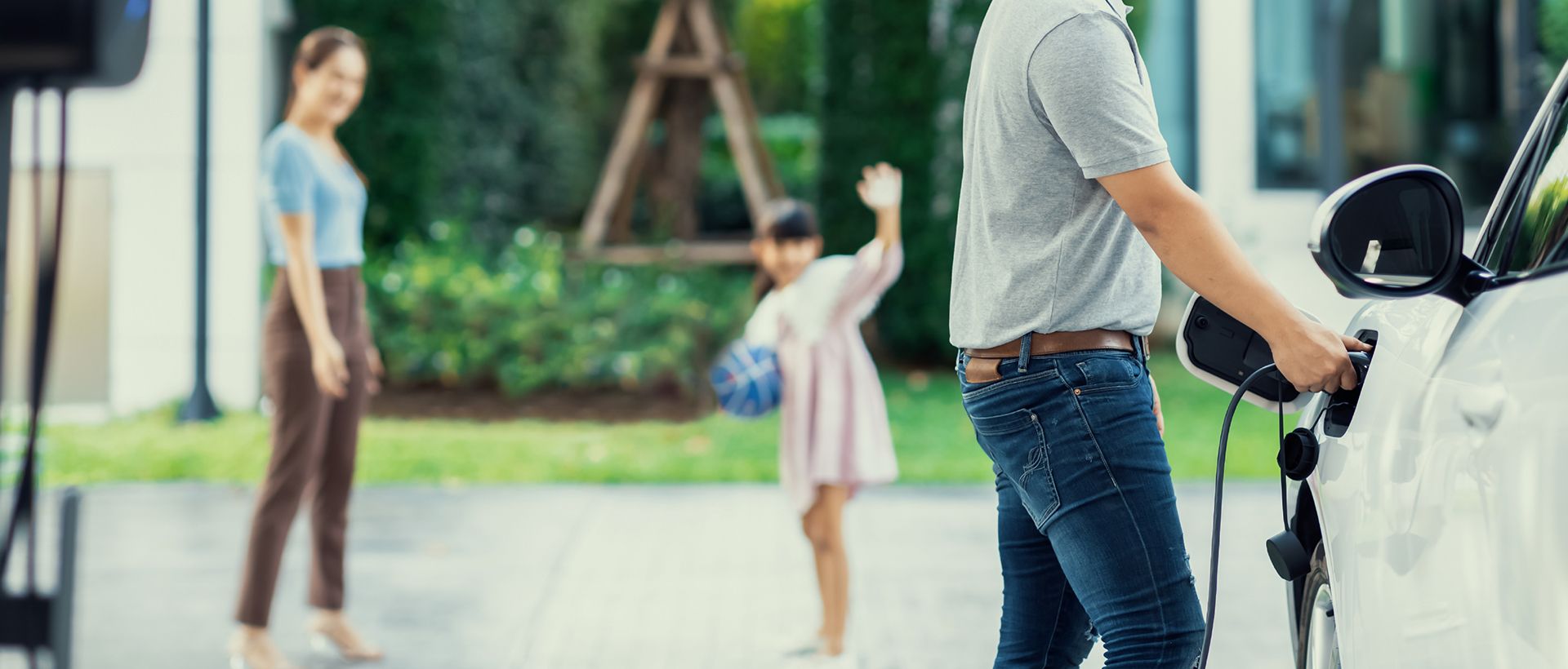 Man laddar elbil hemma med familj i bakgrunden