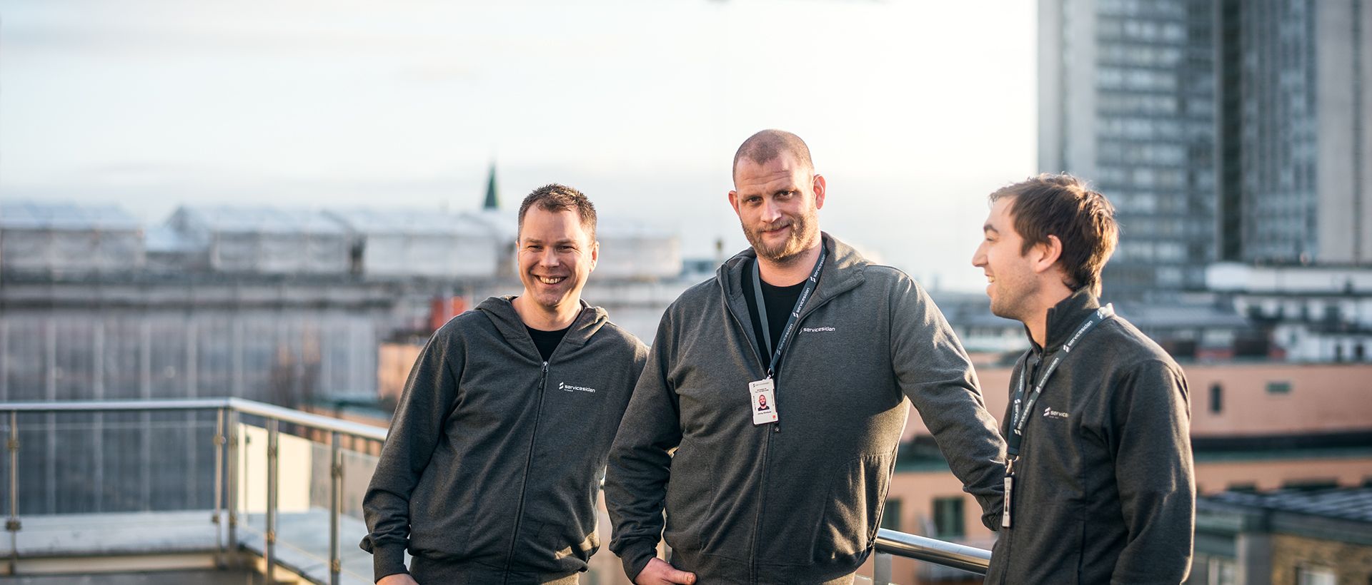 Tre S2 Elektriska-medarbetare på hustak med Stockholms silhuett