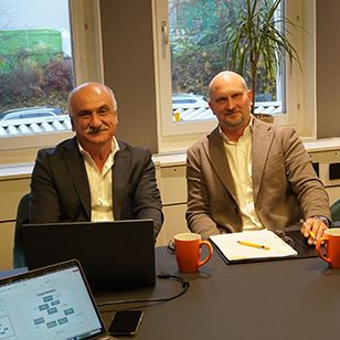 Två representanter diskuterar ISO-certifiering vid mötesbord