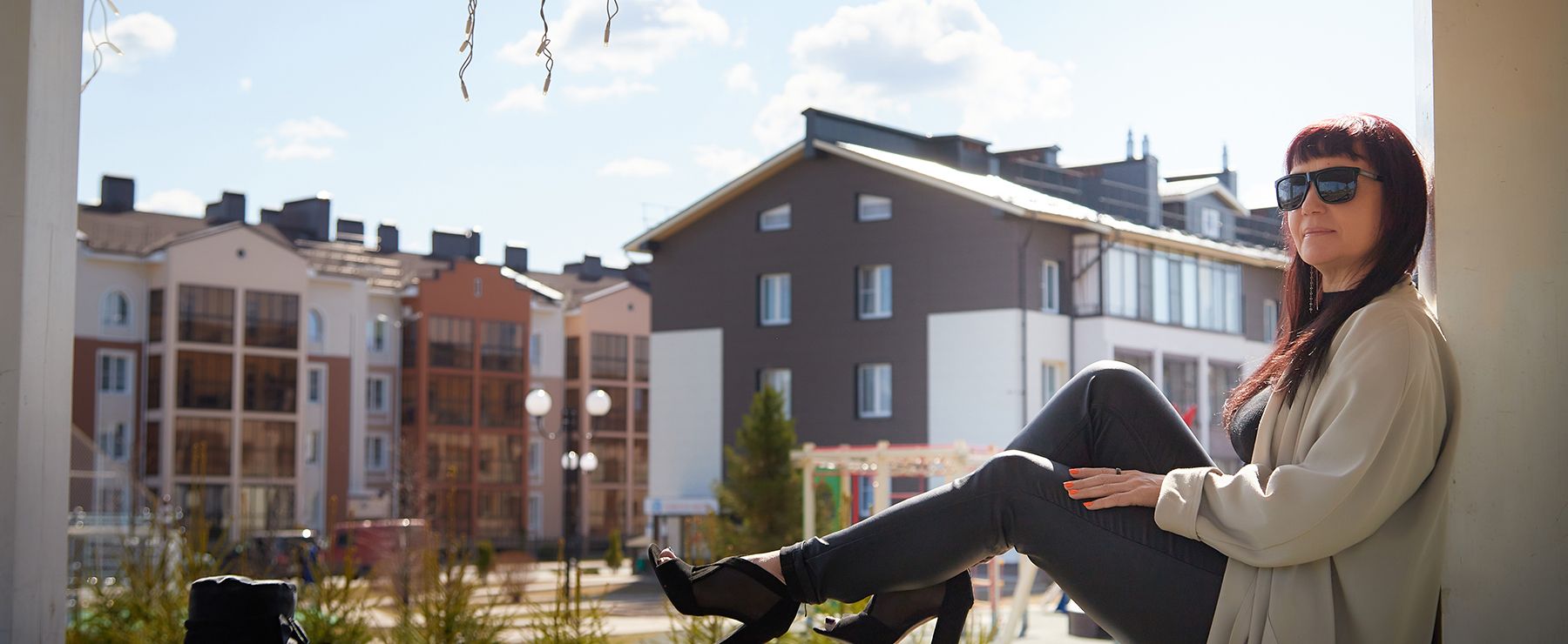 Kvinna sitter avslappnat på balkong framför flerbostadshus